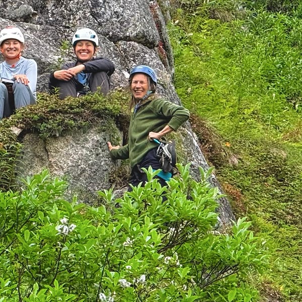 Five WCA climbers in helmets gathered on a ledge partway up an Alaskan crag