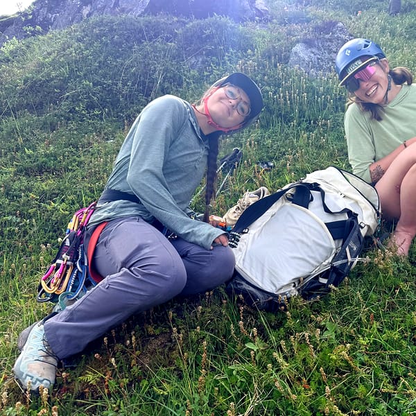Two WCA climbers rest in green tundra after a route, sorting a rope between them