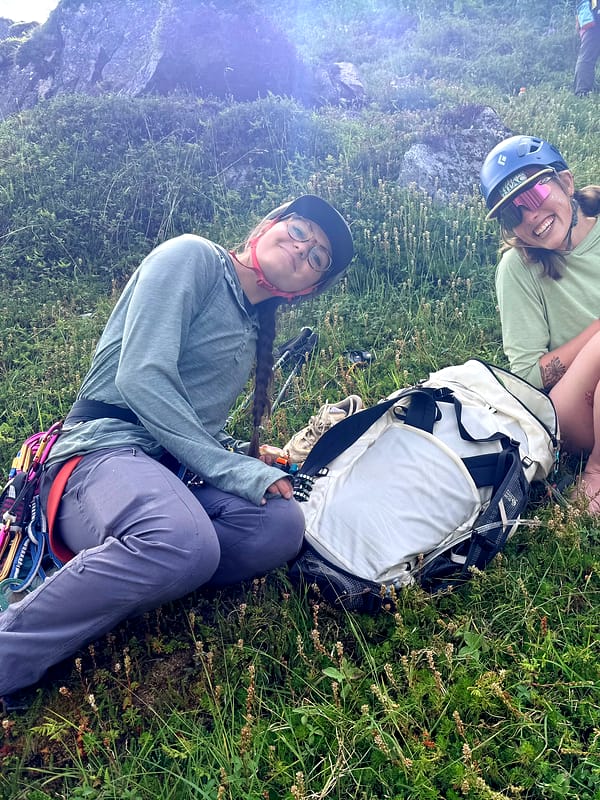 Two WCA climbers sitting in green tundra after a route, laughing as they coil a rope