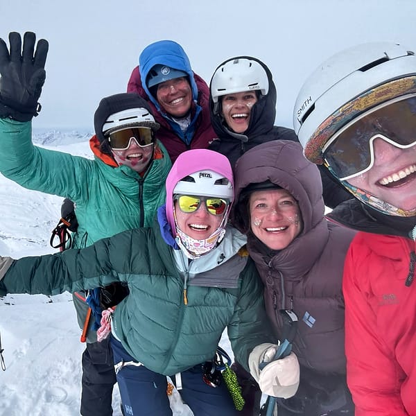 A WCA ski group crowded together laughing on a snowy Alaskan ridge