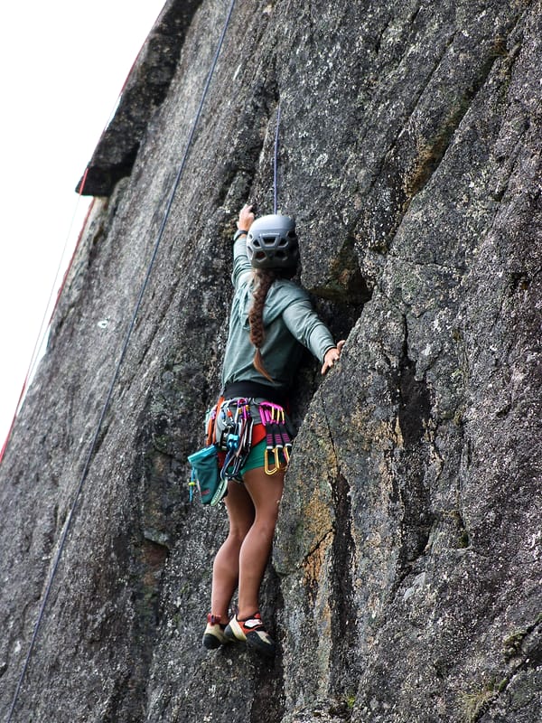 A WCA climber moving up a clean granite slab, a rack of quickdraws on her harness