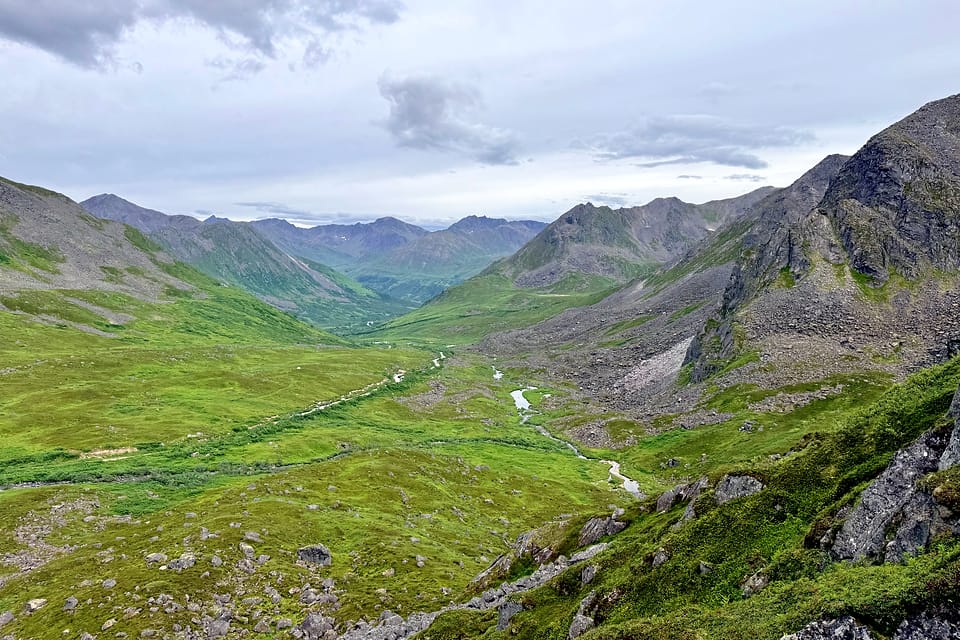 A braided river running through a green Alaskan valley between long ridgelines